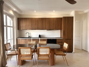 A modern kitchen with wooden cabinets, a black countertop, and a round dining table with six wicker chairs. - - (Cannes)