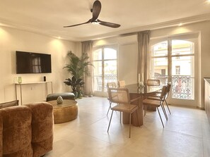 A modern living room with a flat-screen TV, a ceiling fan, a dining table with chairs, a sofa, and a potted plant. - - (Cannes)