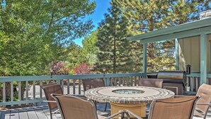 Une terrasse dotée d’une table ronde et de chaises, entourée d’une rambarde en bois, et offrant une vue sur une zone boisée.