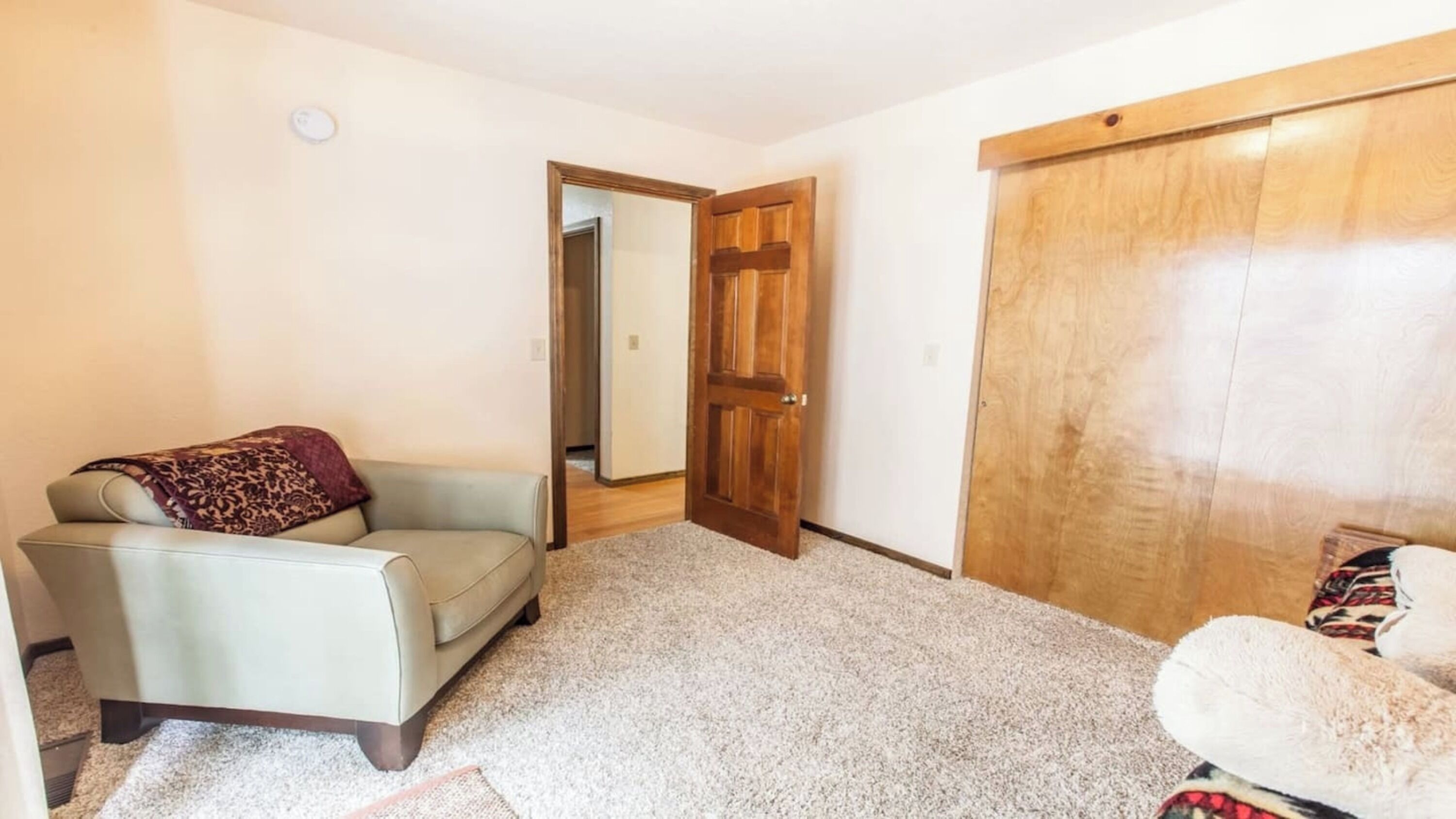 A room with a beige sofa, a wooden door, and a carpeted floor.