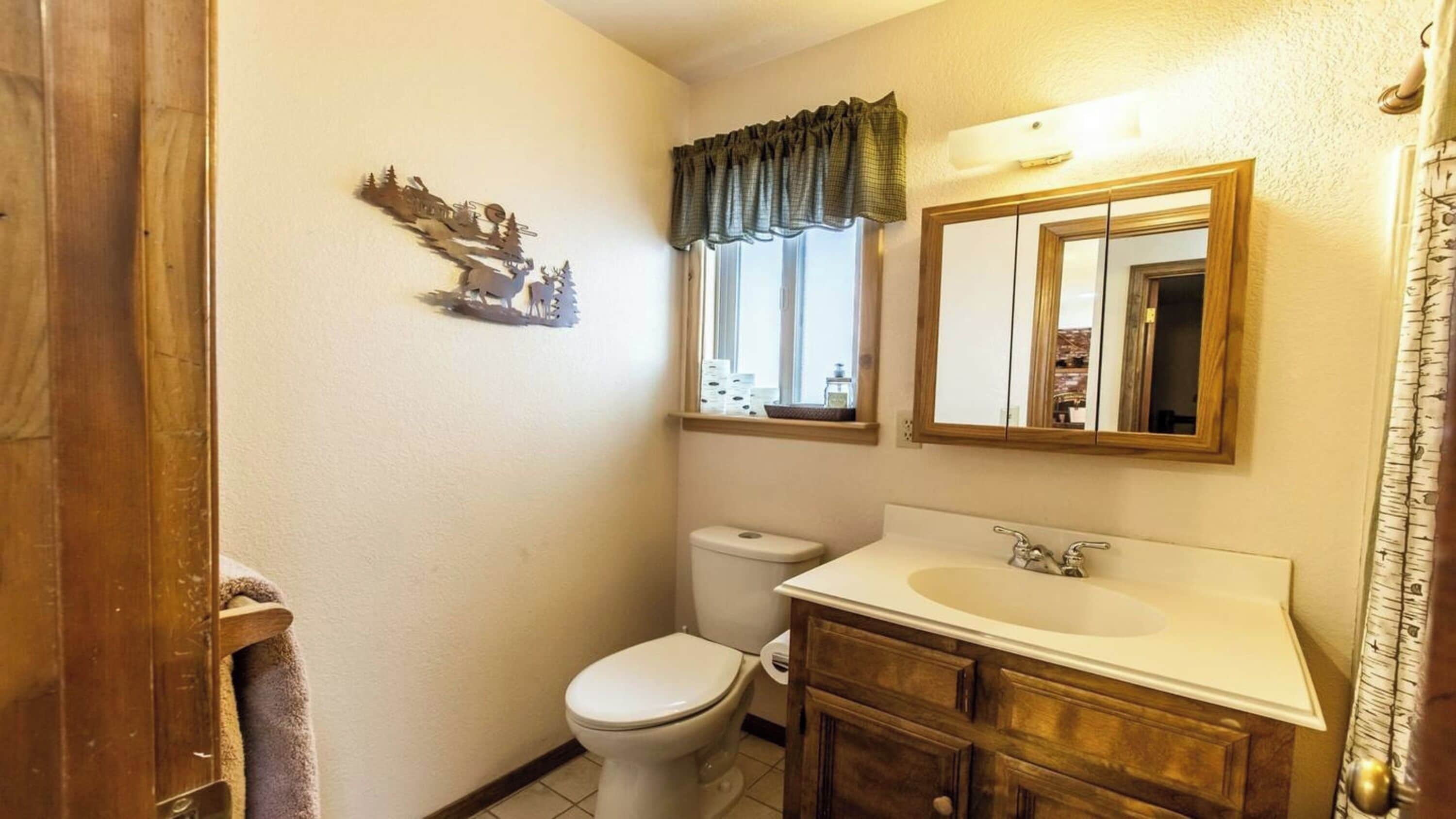 Un baño con inodoro, lavabo, espejo y un recorte decorativo en la pared.