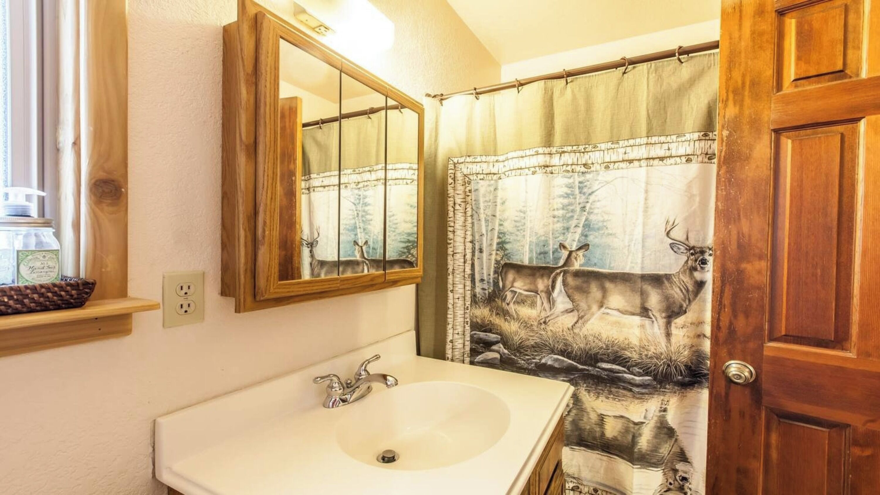 A bathroom with a wooden door, a mirror, a sink, and a shower curtain with a deer print.