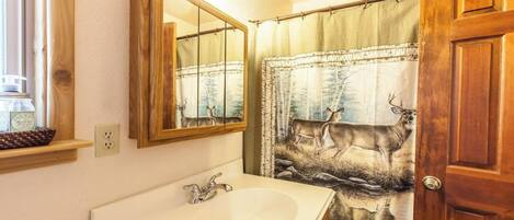 A bathroom with a wooden door, a mirror, a sink, and a shower curtain with a deer print.