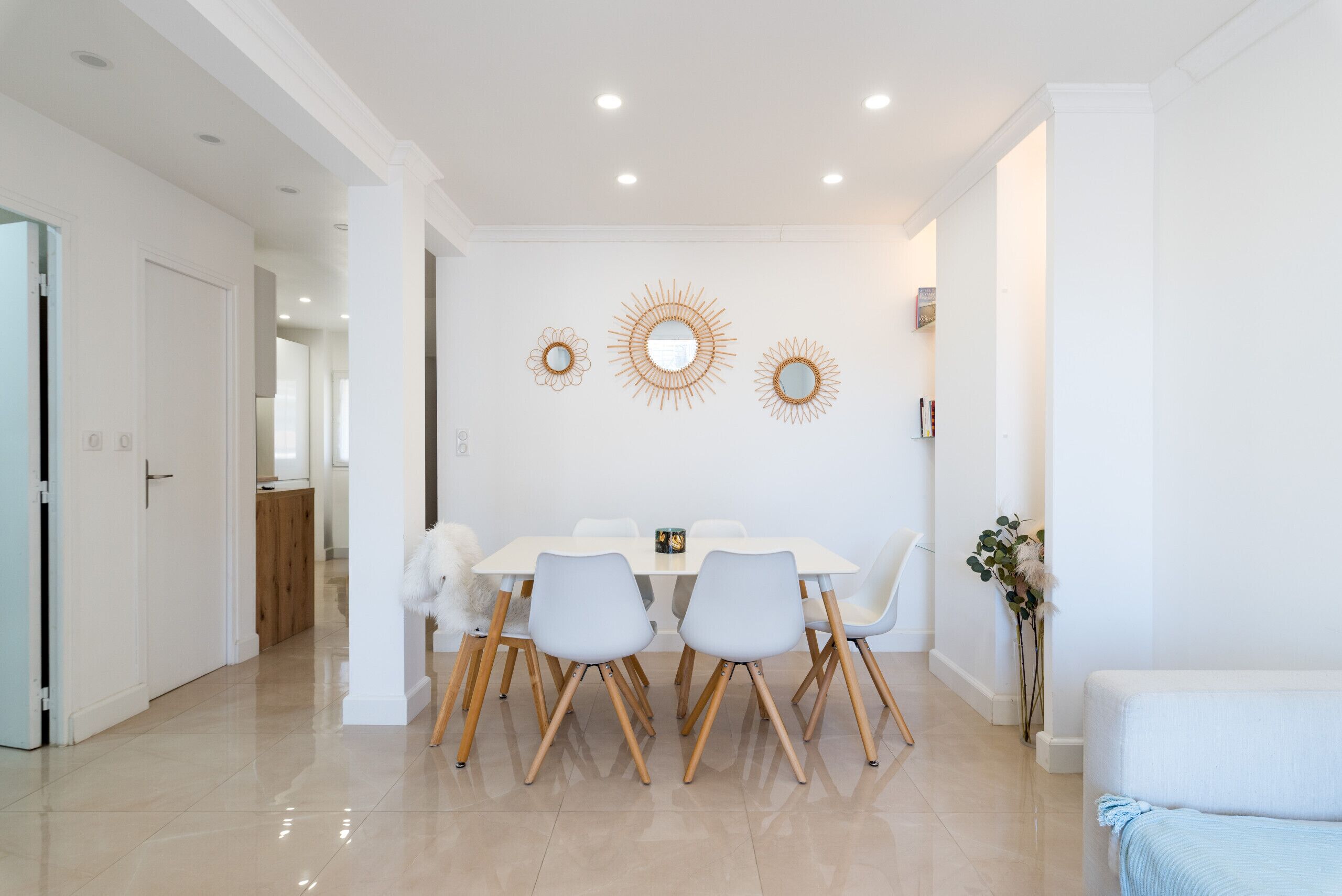 A dining area with a white table and chairs, a mirror, and decorative sunburst wall art.