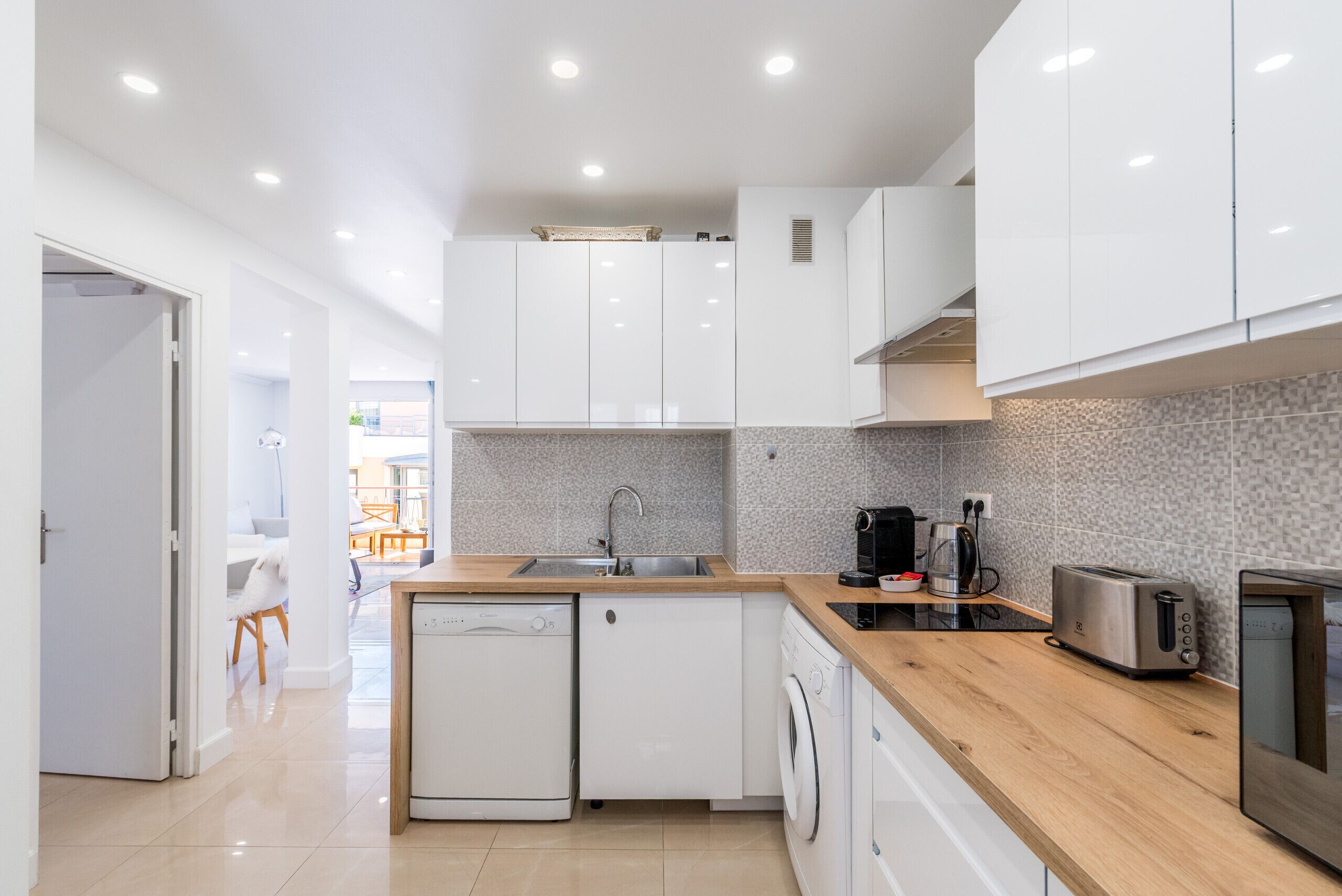 A modern kitchen with white cabinets, a dishwasher, a washing machine, a coffee maker, and a toaster.