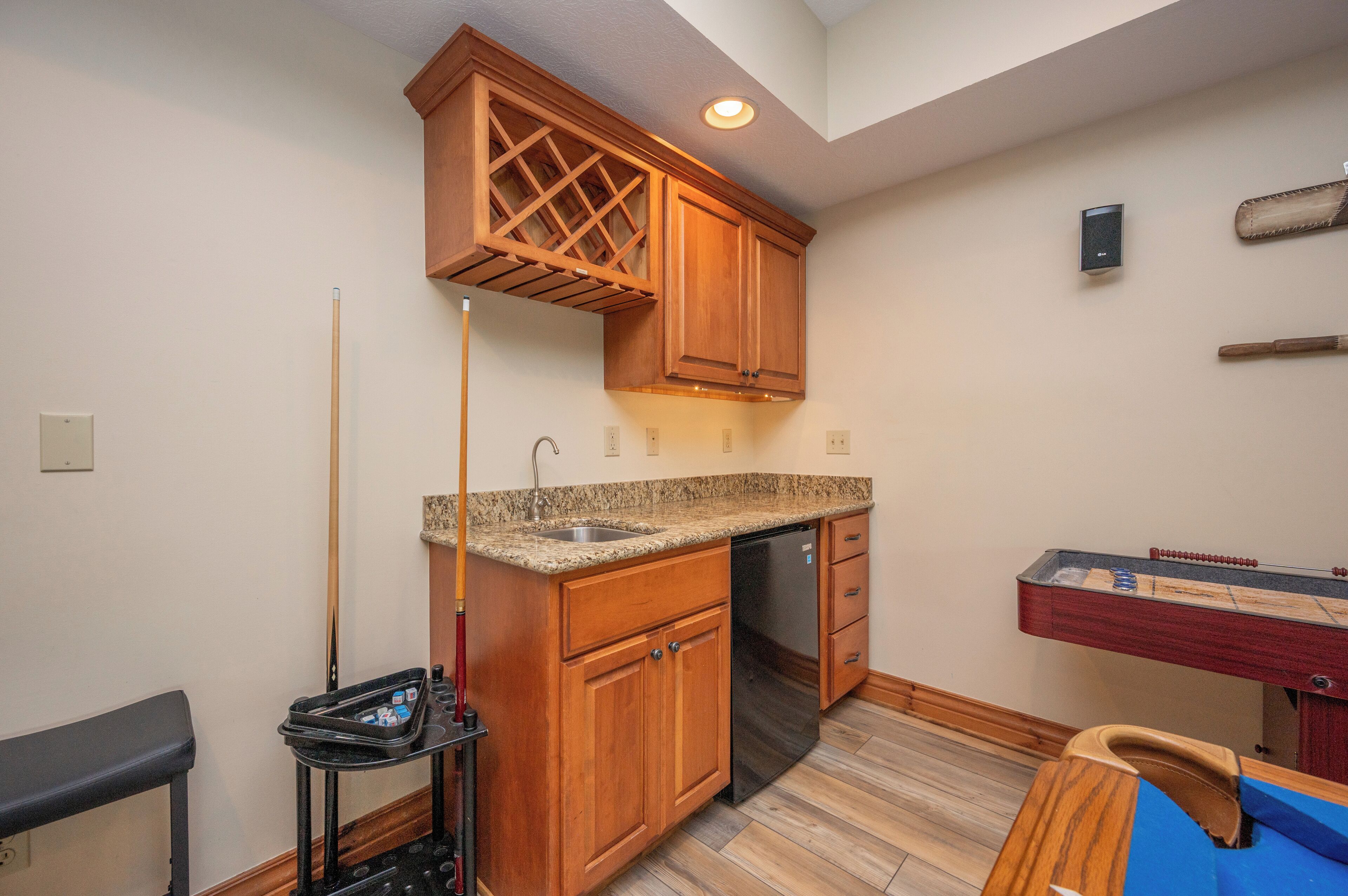 A compact kitchen with wooden cabinets, a built-in dishwasher, a granite countertop, and a ping pong table.