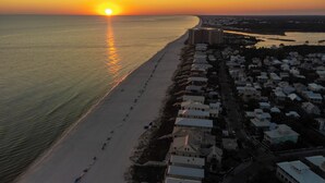 Luftaufnahme einer Küstenstadt mit Strand, Gebäuden und einem Sonnenuntergang.