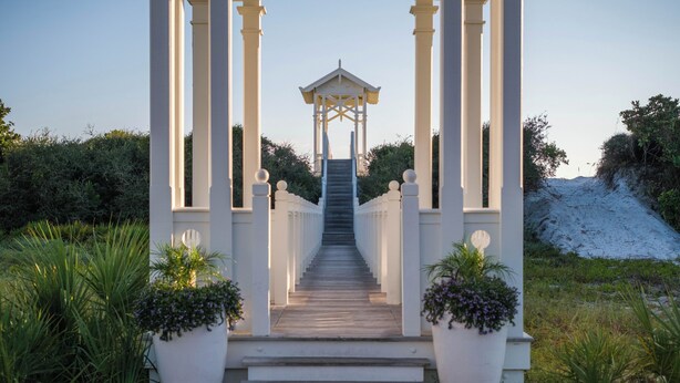 Ein Gazebo mit einer Treppe zu einem überdachten Bereich, umgeben von weißen Säulen und Topfpflanzen.