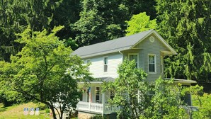 A two-story house with a porch, surrounded by lush greenery and trees.