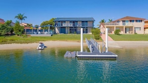 Une propriété située au bord de l’eau, dotée d’un quai, d’un bateau et d’une grande maison avec un toit bleu.