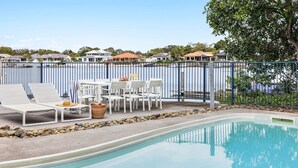 Un espace aménagé au bord de la piscine, avec des chaises longues, une table et un ensemble de mobilier de jardin.
