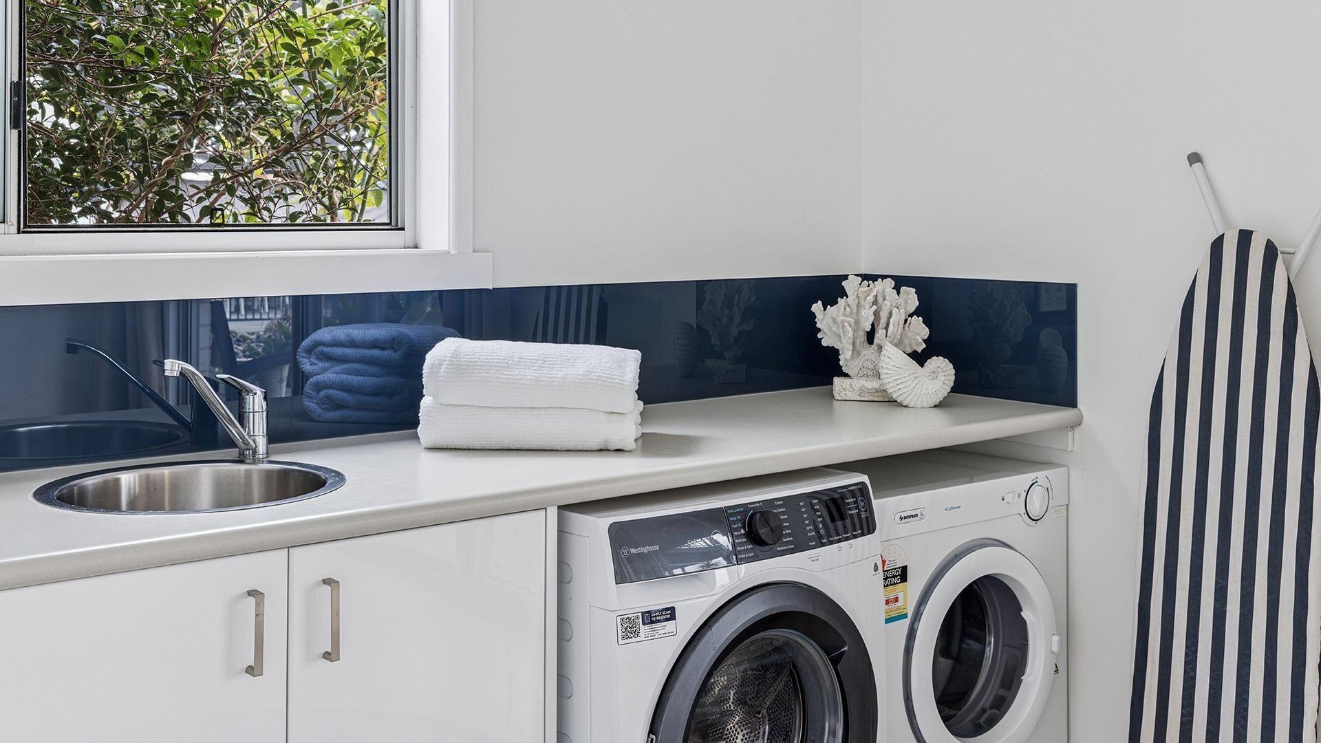 A modern kitchen with a built-in washing machine, a sink, and a window with a view of greenery.