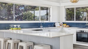 Une cuisine moderne dotée d’un grand îlot central, d’un four encastré et offrant une vue sur les arbres grâce à de grandes fenêtres.