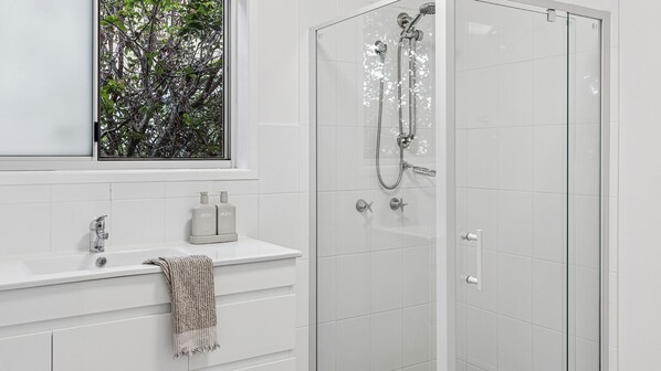 Un baño moderno con cabina de ducha de vidrio, tocador blanco con una toalla y ventana con vistas a árboles.