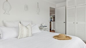 Une chambre à coucher bien rangée, avec un lit, des oreillers, une petite table avec des livres et un chapeau de paille posé sur le lit.