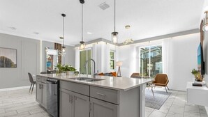 A modern kitchen with a central island, stainless steel appliances, pendant lighting, and a view to the dining area.