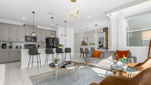 A modern apartment with a kitchen, dining area, and living room. It features contemporary furniture, pendant lighting, and a large window providing natural light.