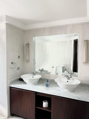 A bathroom with two sinks, a large mirror, and a dark wood vanity. - Villagio (Accra)