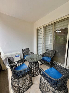 A balcony with wicker furniture, a glass table, and a white air conditioning unit. - Villagio (Accra)