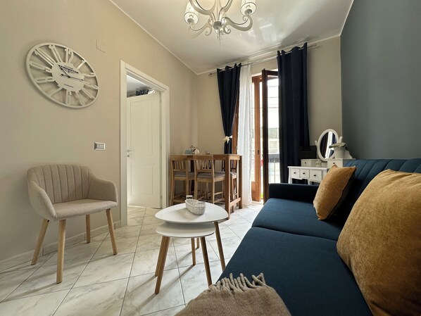 A living room with a sofa, a chair, a dining table, and a decorative clock.