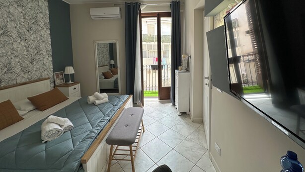A hotel room with a bed, a bench, a TV, and a view of the outside. - Provencal style suite (second floor) (Licata)