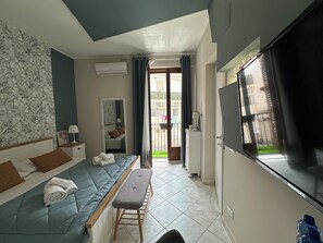 A hotel room with a bed, a bench, a TV, and a view of the outside.