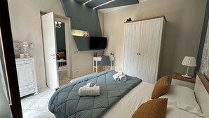 A bedroom with a bed, a desk, a wardrobe, a TV, and a bathroom visible through an open door. - Provencal style suite (second floor) (Licata)