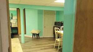 Una habitación con paredes verde azulado, suelo de madera, una puerta, un microondas, una silla y un taburete pequeño.