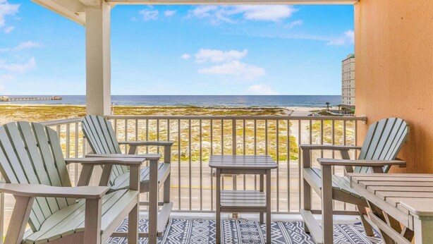 Un balcón con sillas Adirondack y una pequeña mesa, con vistas a una playa y el océano.