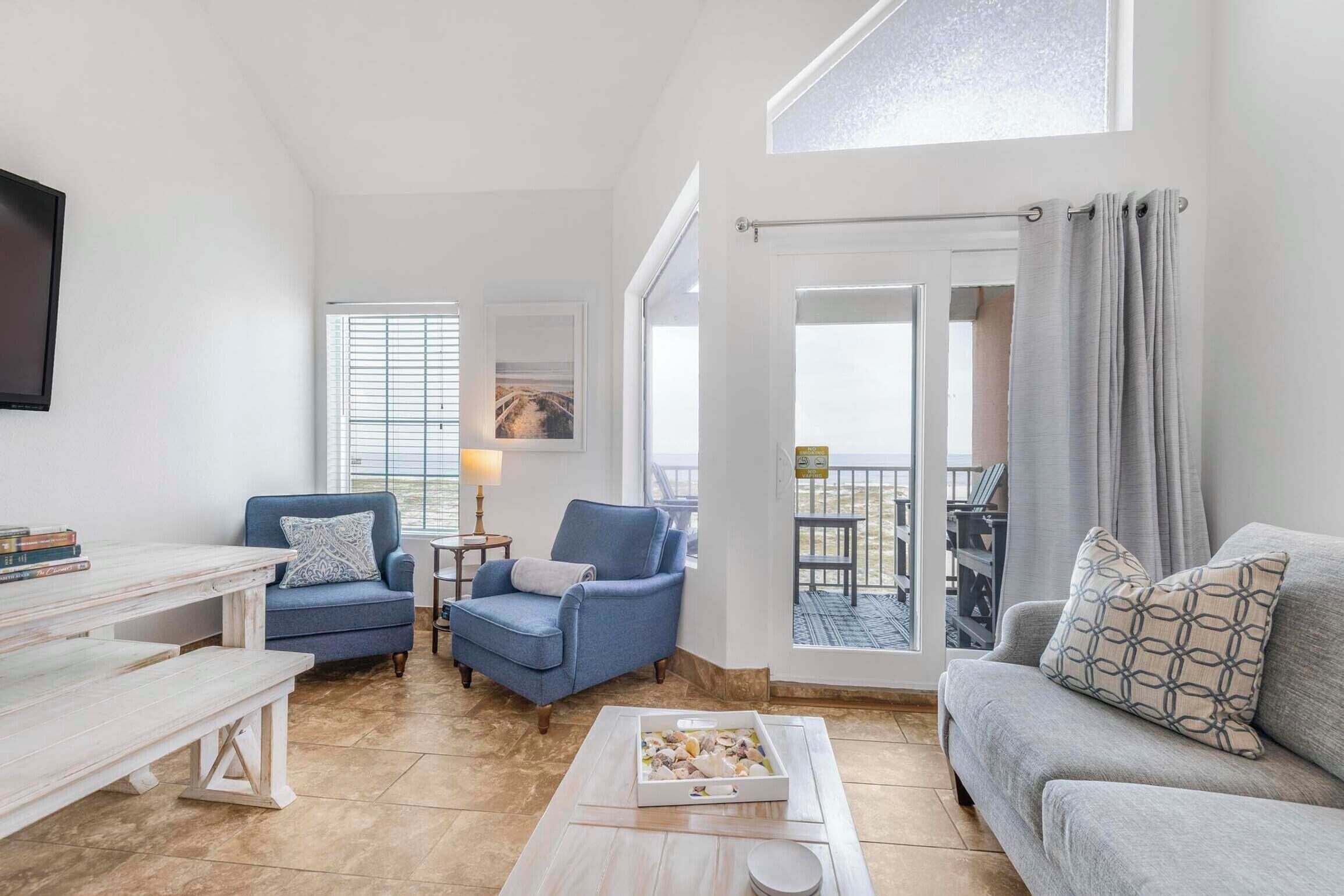 A modern living room with a blue sofa, a grey sofa, a coffee table with a box of snacks, and a TV on the wall.