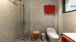 A modern bathroom with a glass shower enclosure, a toilet, and a small wooden stool.
