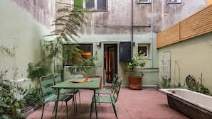 A small courtyard with a table and chairs, surrounded by potted plants and a wooden bench.