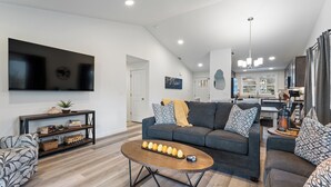 A modern living room with a grey sofa, a coffee table, and a TV mounted on the wall. - Pirates Cove | Glamping-Style Escape with Dock, Cabins & River Access (Orondo)