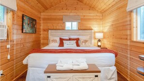 A wooden cabin bedroom with a bed, pillows, a bedside lamp, and a window. - Pirates Cove | Glamping-Style Escape with Dock, Cabins & River Access (Orondo)