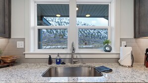 A kitchen with a granite countertop, stainless steel sink, and a window with a view of snow-covered trees. - Pirates Cove | Glamping-Style Escape with Dock, Cabins & River Access (Orondo)