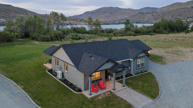 A two-story house with a dark roof, a covered porch, and a well-maintained lawn. - Pirates Cove | Glamping-Style Escape with Dock, Cabins & River Access (Orondo)