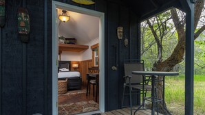 A cozy cabin with a wooden deck, a small dining area, and a bedroom with a bed and a desk. - Pirates Cove | Glamping-Style Escape with Dock, Cabins & River Access (Orondo)