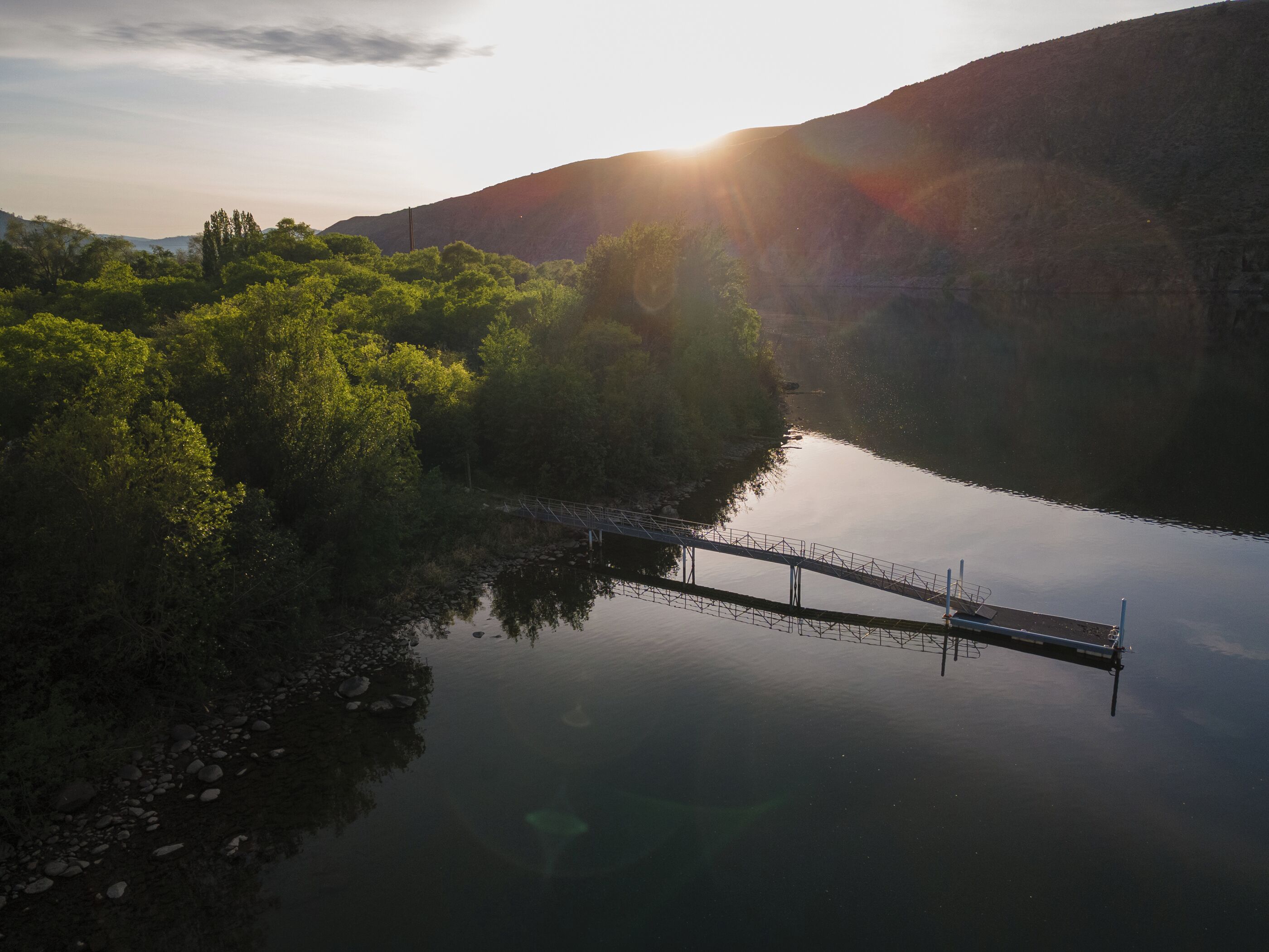 Um rio calmo com uma ponte, cercado por vegetação densa e colinas.