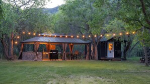 A rustic outdoor dining area with a covered pavilion, string lights, and a small cabin.