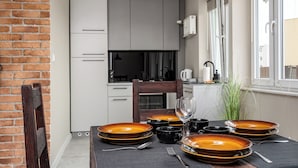 Una cocina moderna con armarios blancos, una mesa de comedor con platos naranjas, tazas negras y cubiertos.