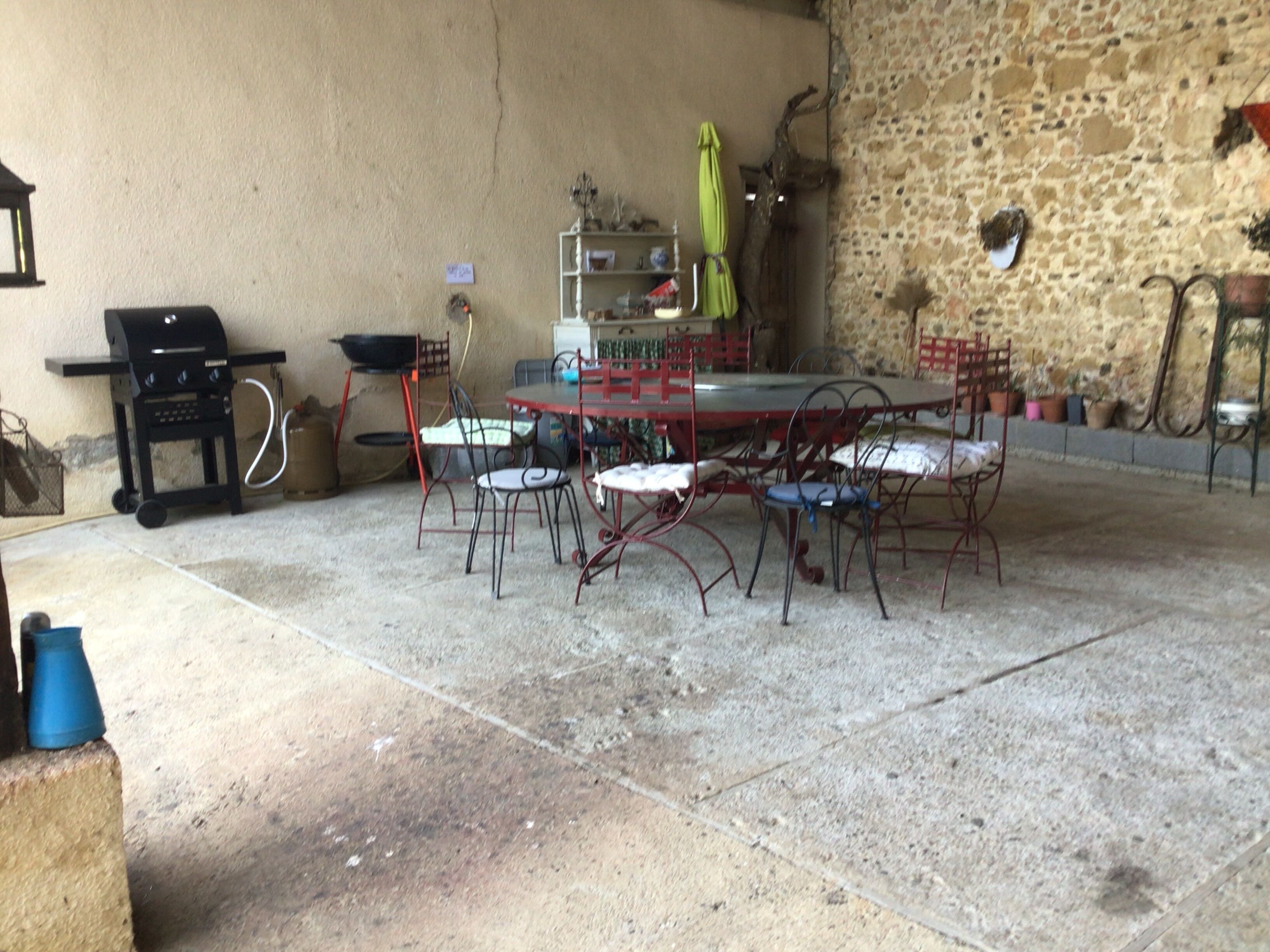 Una terrazza esterna con un muro in pietra, un barbecue e un tavolo da pranzo con sedie.