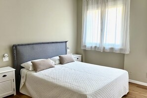 Une chambre à coucher avec un lit, des tables de chevet et une fenêtre ornée de rideaux légers.