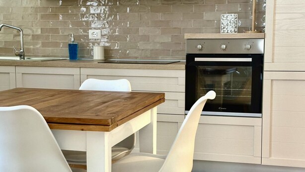 Une cuisine avec une table en bois, des chaises blanches, un évier et une cuisinière.