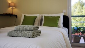 Een net opgemaakt bed met witte en groene kussens, een opgevouwen handdoek en een bedlampje.