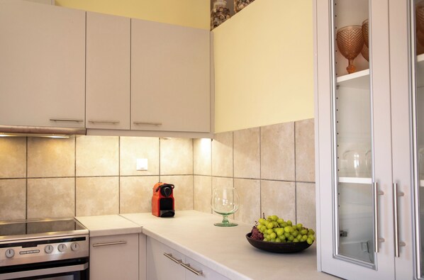 A kitchen with white cabinets, a gas stove, a microwave, a glass wine decanter, and a bowl of green grapes on the counter. - Villa Eleonora Aegina (Aegina)