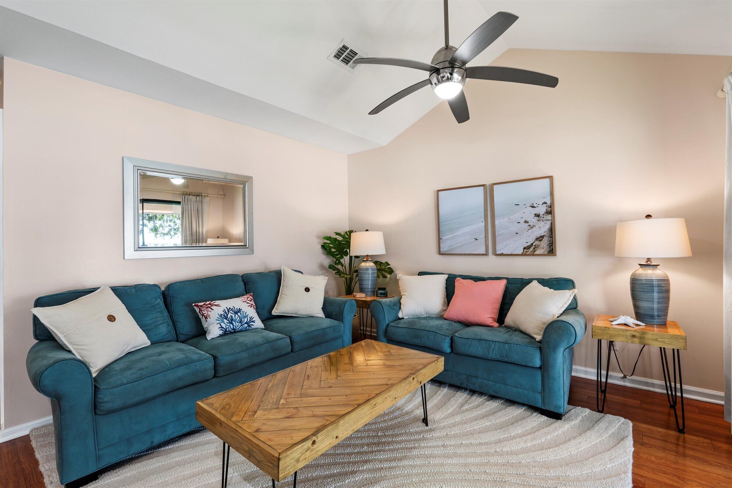 Ein Wohnzimmer mit türkisfarbenen Sofas, einem Holztisch, einem Deckenventilator und zwei Wandleuchten.