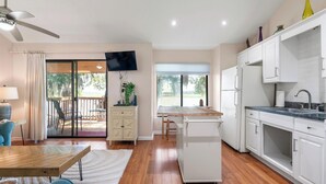 A modern kitchen with white cabinets, a wooden countertop, and a built-in refrigerator. There is a dining area with a table and chairs, and a sliding glass door leading to a patio.
