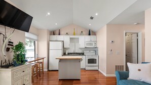 A compact kitchen with white cabinets, a microwave, and a stove. There is a wooden dining table and chairs, a small island with a sink, and a blue sofa in the living area.