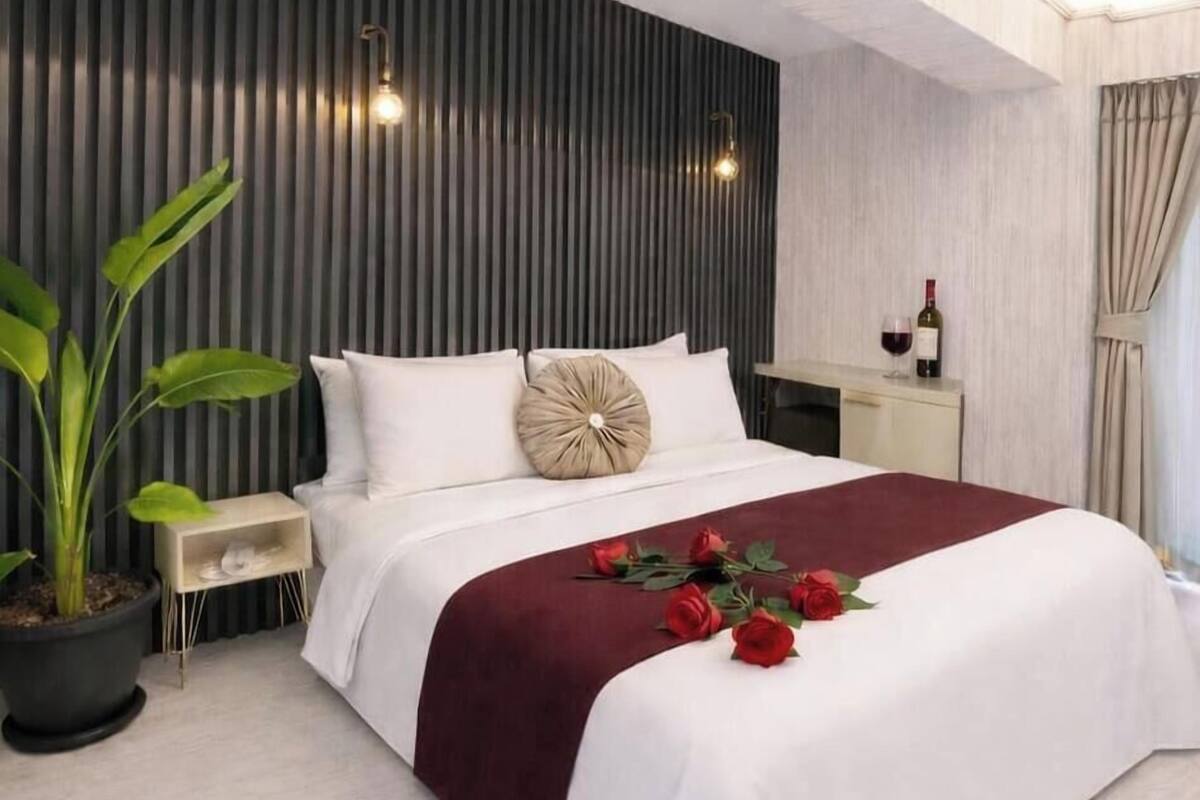 Un dormitorio de hotel moderno con una cama grande, una mesita de noche, una planta en maceta y una botella de vino sobre la mesita.