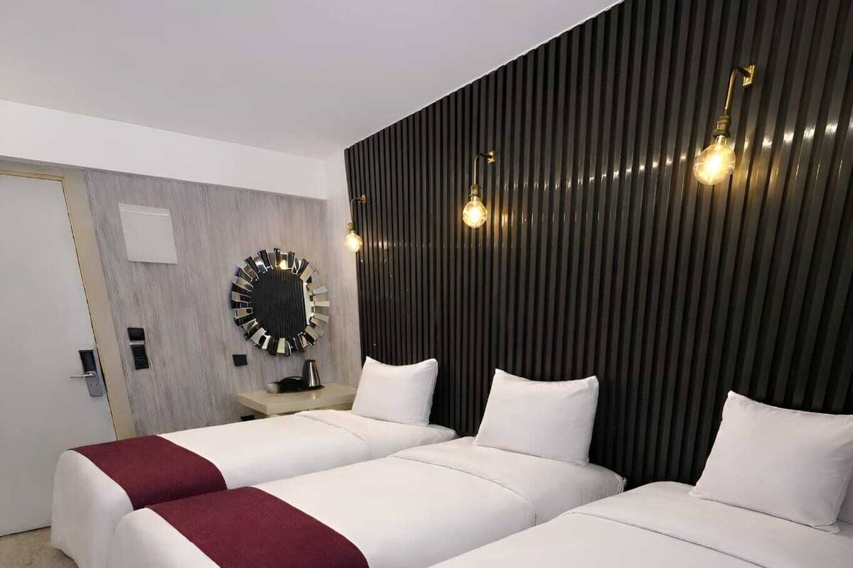 Habitación de hotel con dos camas, piso de madera, diseño moderno en la pared y un espejo redondo.